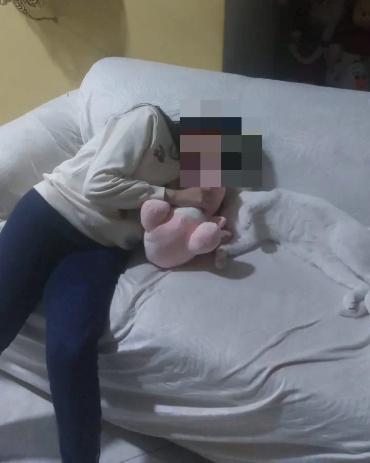 Joven con el rostro pixelado abrazando a Nebu Unicornio junto a su gato